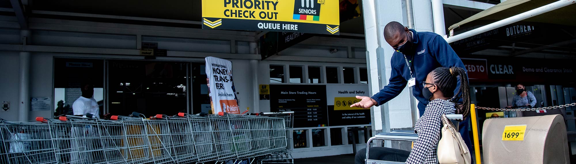 A Makro associate helps a customer in a wheelchair outside a store.